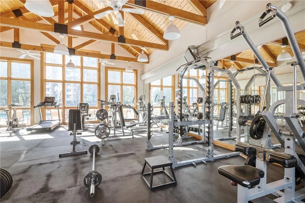 Exercise room with high vaulted ceiling, ceiling fan, a wood ceiling with exposed beams, and healthy amount of natural light