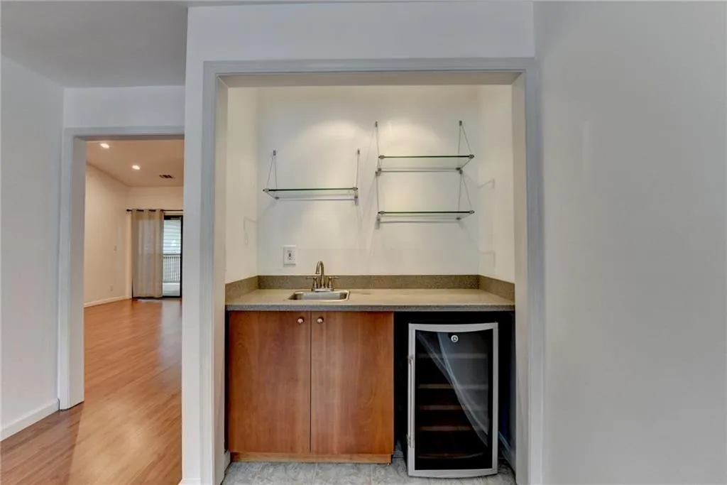 Indoor wet bar with beverage cooler, brown cabinetry, light wood-type flooring, and light stone counters