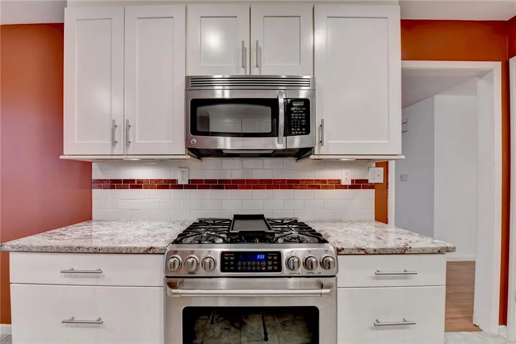 Kitchen featuring stainless steel appliances, white cabinets, light stone counters, and backsplash