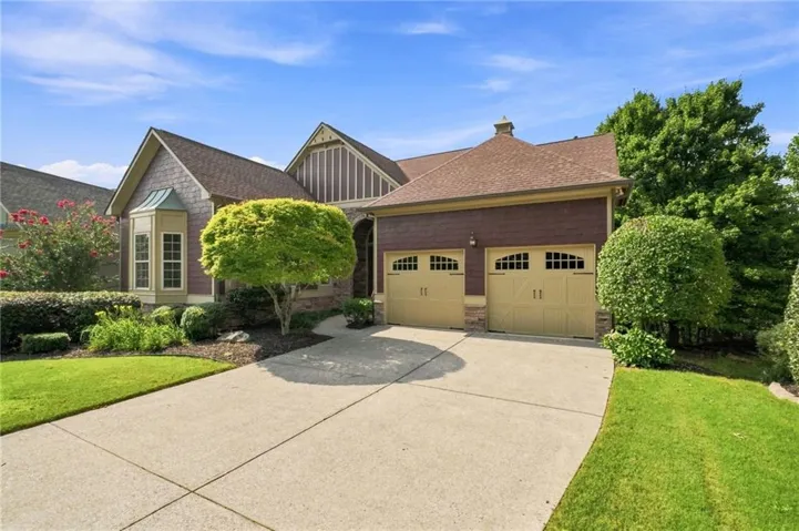 Two-car garage with arched window detailing, an asphalt shingle roof, bay window, landscaped front yard, and concrete driveway