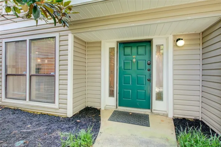 Entryway featuring a paneled green door with sidelight windows, a covered porch, an exterior sconce, and horizontal siding