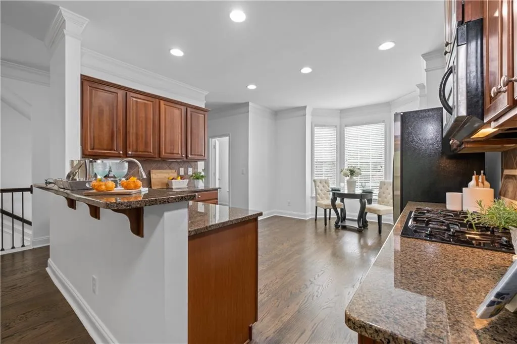 Open concept features a spacious designed kitchen with stained wood cabinets, tasteful backsplash, hardwood floors, a breakfast bar, eat-in kitchen, granite counters, and ornamental molding.