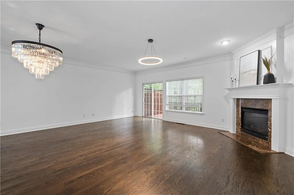 Unfurnished spacious open layout featuring living and dining room spaces with crown molding, hardwood floors, a gas fireplace, and elegant lighting with easy access to the private deck.