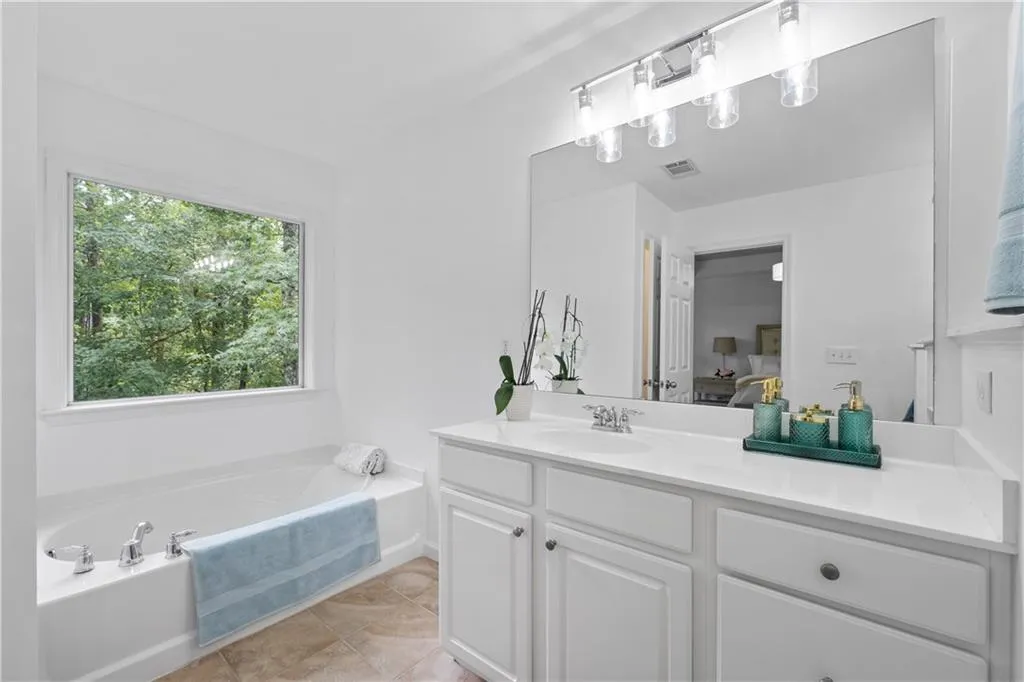 Spacious ensuite bathroom featuring modern light fixtures, soaking tub, two vanities, and abundant light from large, oversized window.