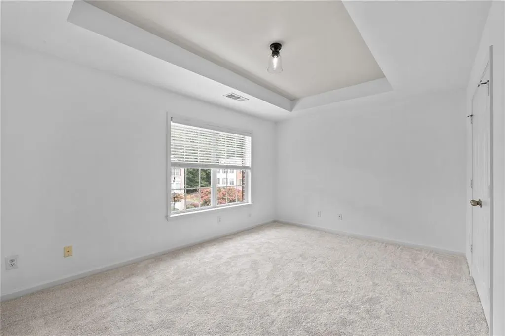 Unfurnished second floor ensuite featuring a trey ceiling, light carpet and large expansive window bringing in natural light.
