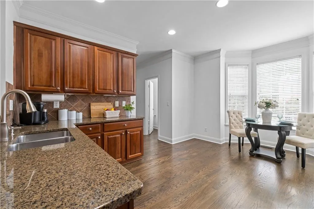 Charming kitchen with recessed lights, spacious breakfast area, granite counters, ornamental molding, tasteful backsplash, stained cabinets and bay window providing views of the outside and natural light.