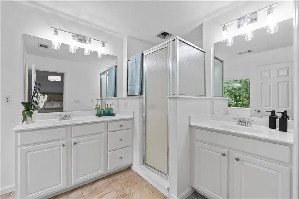 Spacious primary ensuite bathroom featuring a separate shower, two vanities, tiled floors and natural light.