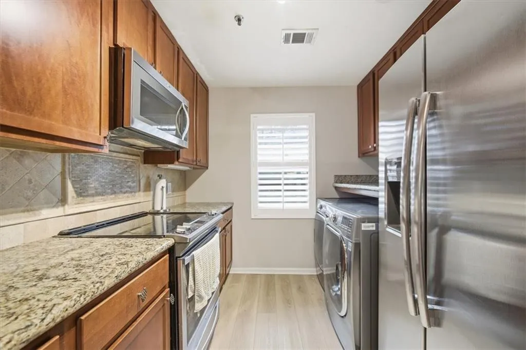Kitchen with appliances with stainless steel finishes, brown cabinets, light wood finished floors, light stone counters, and backsplash