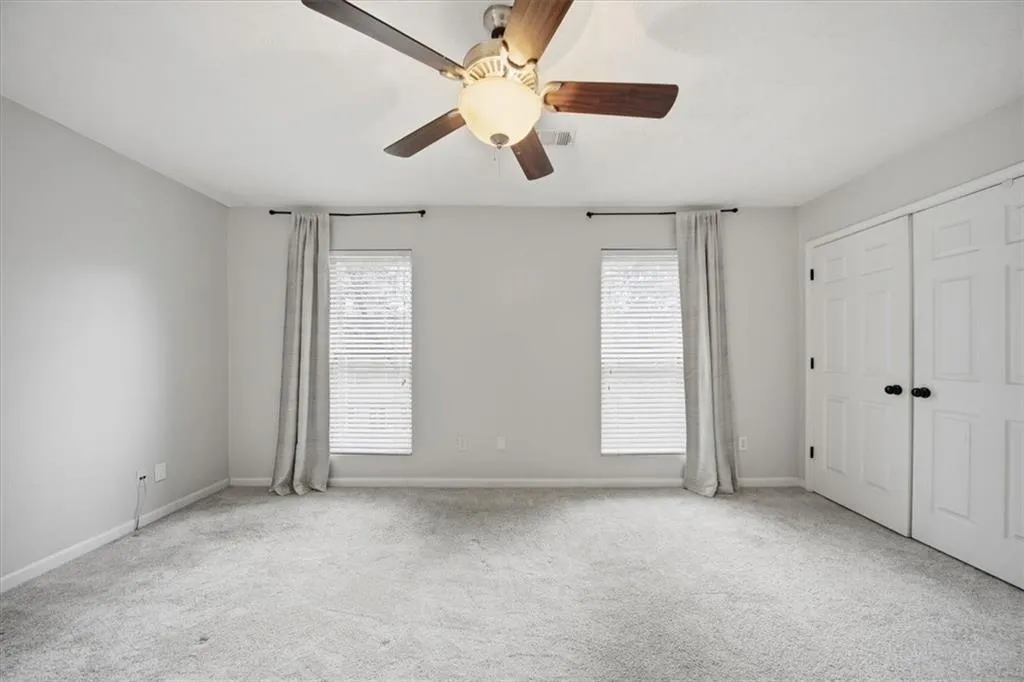 Unfurnished bedroom with multiple windows, light carpet, ceiling fan, and a closet