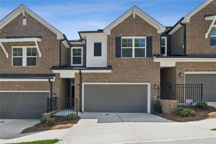Modern brick townhome community featuring three distinctive architectural styles with peaked rooflines, wide driveways with two-car attached garages, and manicured landscaping with fresh mulch beds throughout the streetscape