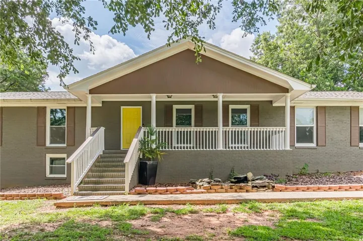 Brick exterior with a covered front porch, white railings, and a contrasting yellow entry door