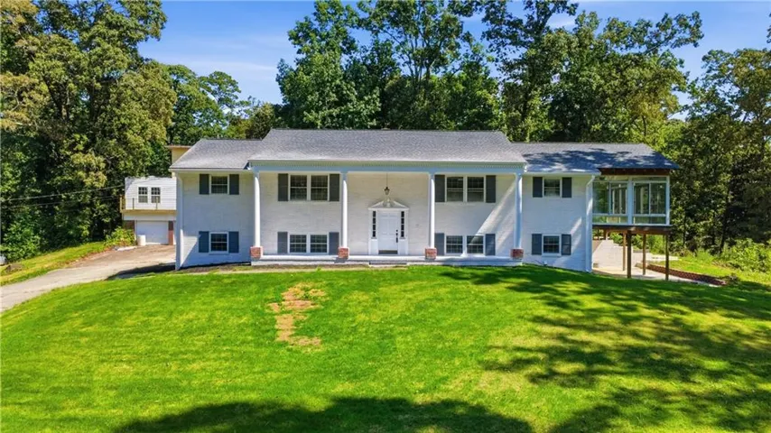 White-painted brick exterior with a columned portico, a screened porch, and a gravel driveway