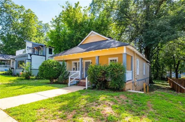 Front exterior featuring a yellow siding facade, covered porch with white railing, and a concrete walkway