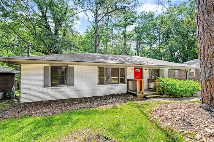 White brick exterior with a red front door and a natural wood porch featuring railings