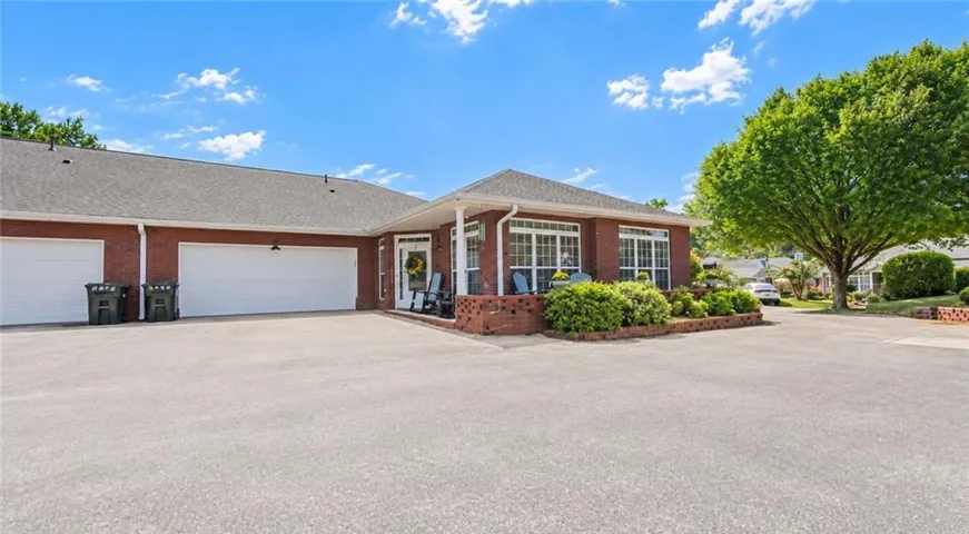 Brick exterior featuring multiple garage bays, a covered porch, and mature landscaping