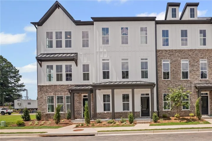 Three-story townhome with brick and vertical siding facade, multiple dormer windows, covered entry porch, and dark-framed windows