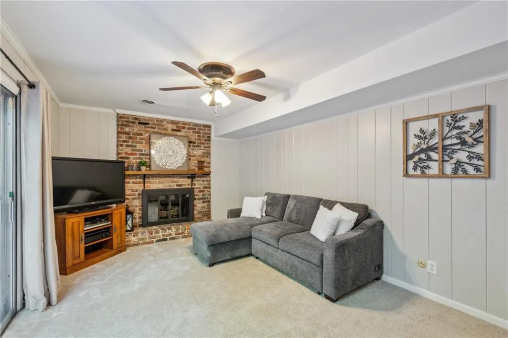 Carpeted living room featuring a fireplace, a ceiling fan, wooden walls, and crown molding