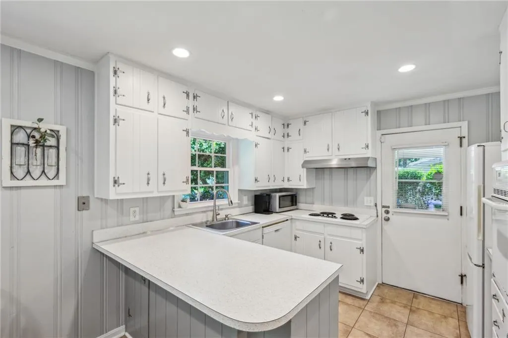 Kitchen with white cabinetry, a peninsula, light countertops, light tile patterned flooring, and white appliances