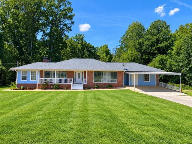 Brick and siding exterior with a covered front porch, attached carport, and mature trees