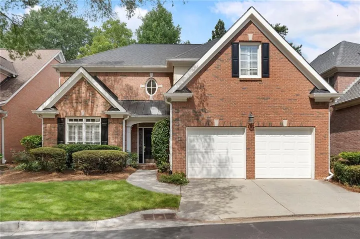 Brick facade home featuring a two-car garage, established front landscaping, an oval window accent, and black louvered shutters