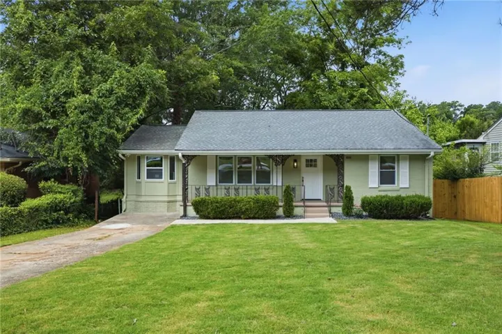 Front exterior featuring a covered porch with decorative iron railings, a gabled roof, and light green siding with white window shutters