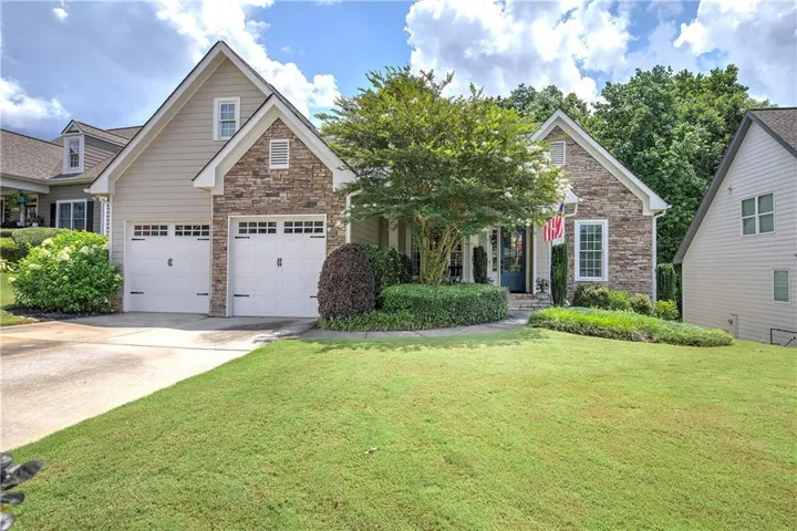 Stone and siding exterior featuring an arched entry, a two-car garage with carriage-style doors, and established front landscaping