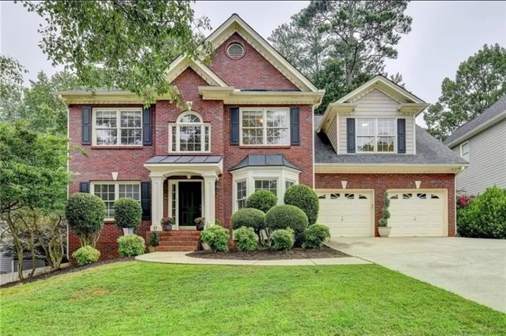 Brick exterior with white trim, two-car garage, manicured shrubs, and a paved driveway