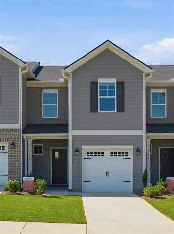 Modern townhome featuring a one-car garage with carriage-style doors, gray fiber cement siding, and a gabled roofline