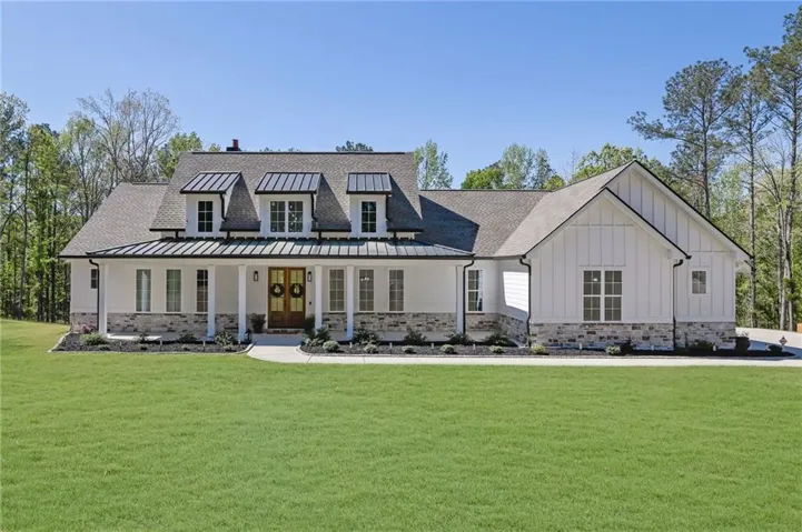Modern farmhouse style home with a porch, view of wooded area, and board and batten siding