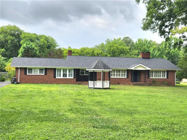 Brick exterior with multiple windows, a dark shingle roof, and two chimneys