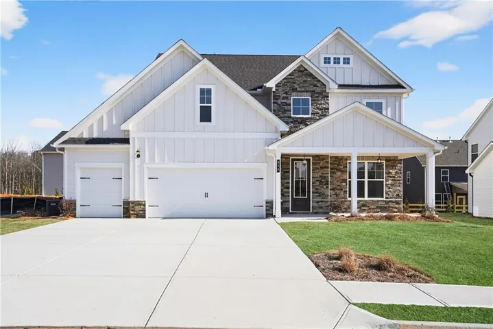 Contemporary exterior featuring white board and batten siding with stone accents, a covered front porch, an attached two-car garage, and a single-car garage