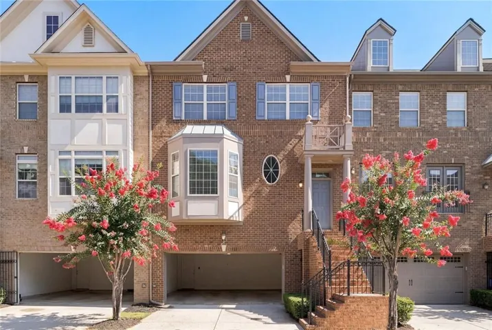 Brick townhome featuring a two-car garage, bay window, exterior balcony, and gabled dormers