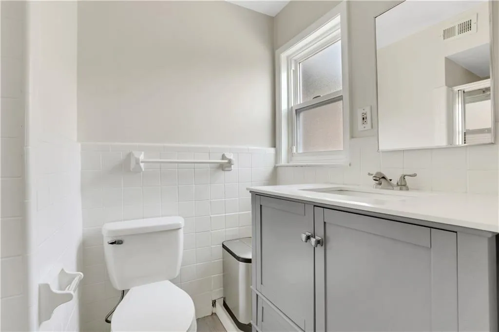 Bathroom featuring toilet, tile walls, vanity, and a wainscoted wall