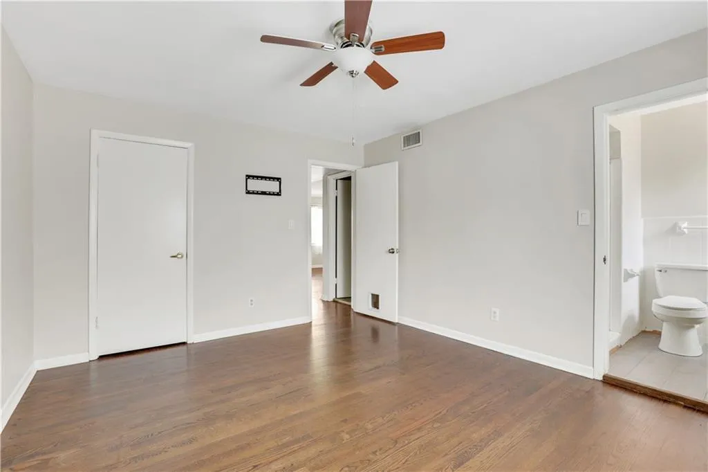Unfurnished bedroom with wood finished floors, ensuite bath, baseboards, and ceiling fan