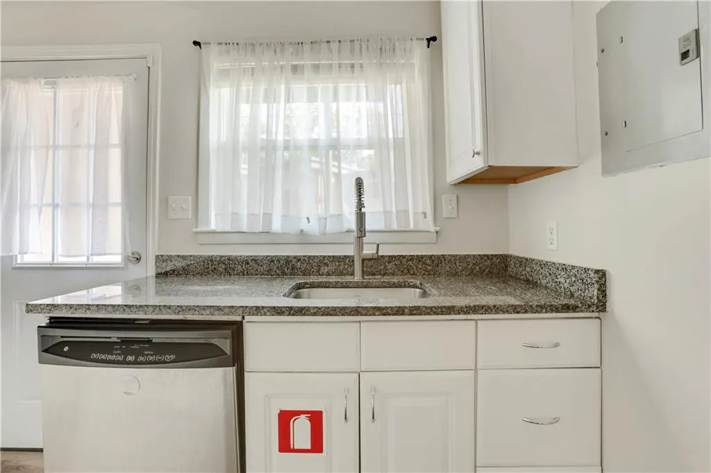 Kitchen with stainless steel dishwasher, a sink, electric panel, and white cabinets