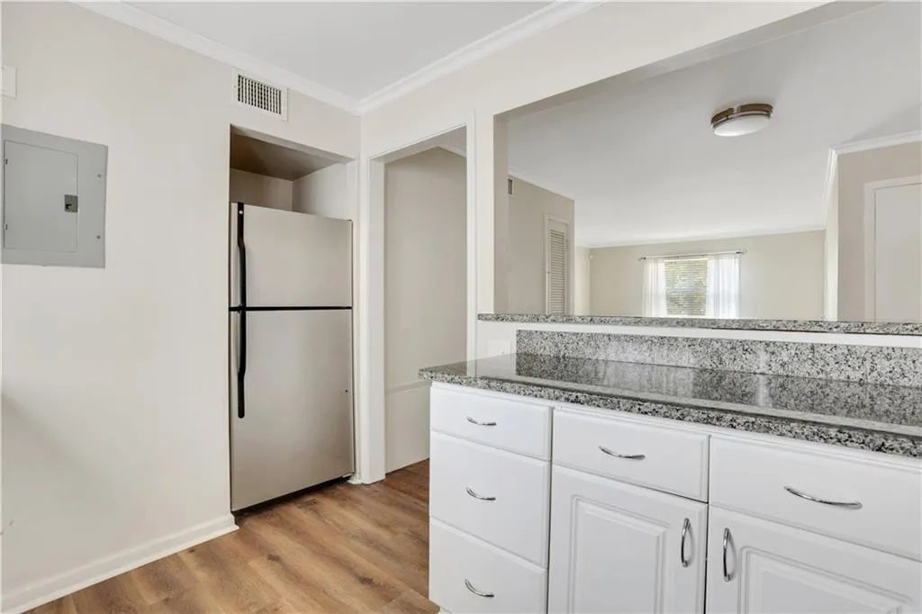 Kitchen with freestanding refrigerator, electric panel, ornamental molding, light wood-type flooring, and white cabinetry