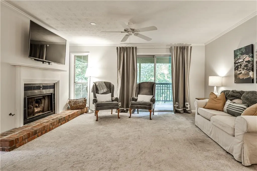 Carpeted living area with crown molding, a fireplace with raised hearth, a textured ceiling, and ceiling fan
