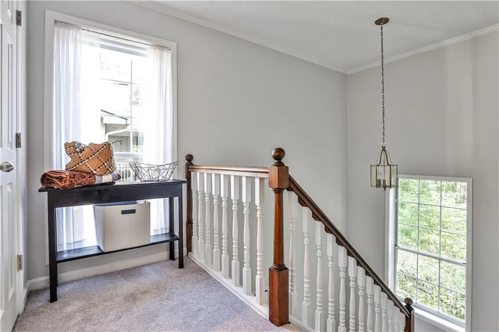 Hallway featuring light carpet, an upstairs landing, ornamental molding, and a chandelier