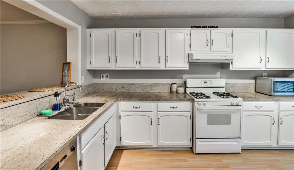 Kitchen with gas range gas stove, white cabinets, stainless steel microwave, light wood finished floors, and under cabinet range hood