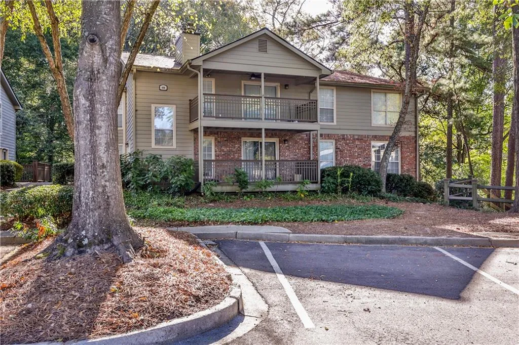 View of front of home featuring brick siding, uncovered parking, a chimney, a porch, and a balcony