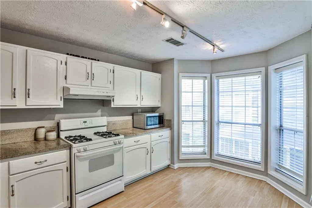 Kitchen featuring track lighting, white range with gas cooktop, light wood-style flooring, white cabinets, and a textured ceiling