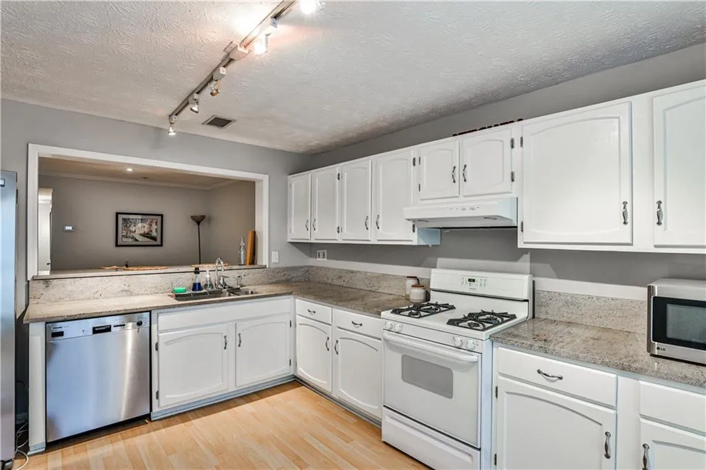 Kitchen with stainless steel appliances, light wood finished floors, white cabinets, track lighting, and under cabinet range hood