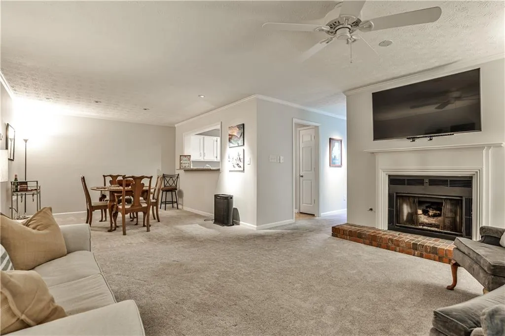 Living room with carpet floors, a fireplace, ornamental molding, a textured ceiling, and a ceiling fan