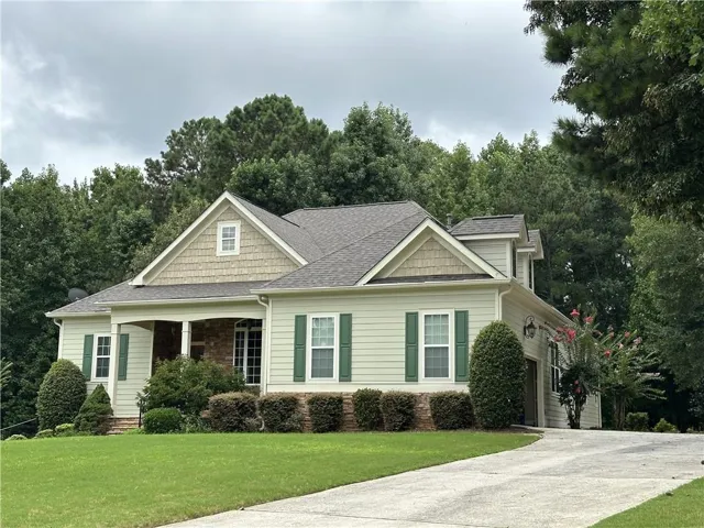 Classic Colonial-style cottage featuring cream-colored fiber cement siding, a gabled roofline with architectural details, and black shutters flanking multi-pane windows