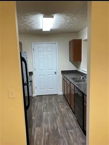 Galley kitchen featuring wood-finish flooring, dark countertops, dark lower cabinetry, and a black appliance suite