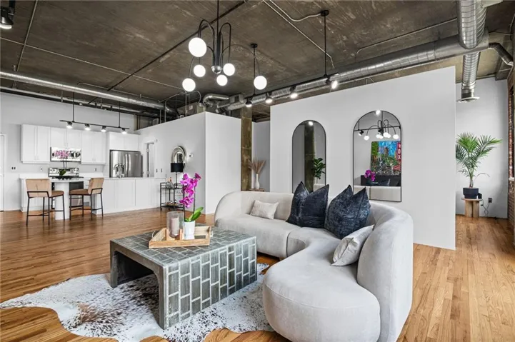Open-concept living space featuring wood-finish flooring, exposed concrete ceiling, industrial-style ductwork, and track lighting