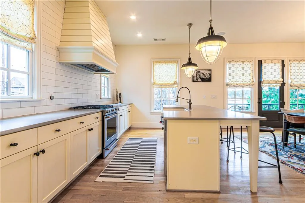 Kitchen with stainless steel stove, light hardwood / wood-style flooring, tasteful backsplash, an island with sink, and premium range hood