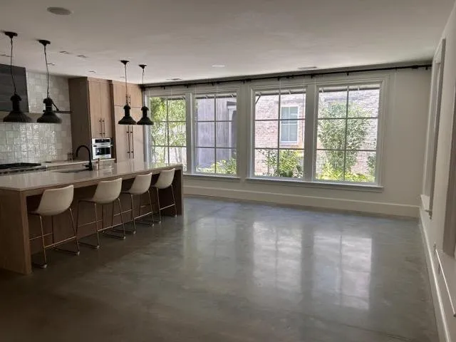 Kitchen featuring stainless steel oven, a sink, baseboards, concrete floors, and decorative backsplash