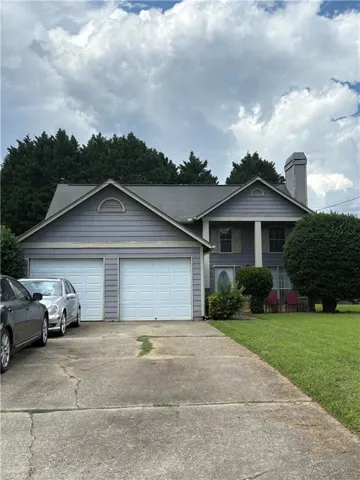 Siding exterior with a two-car garage, concrete driveway, and mature landscaping