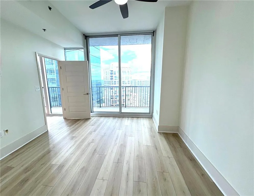 Unfurnished room featuring floor to ceiling windows, healthy amount of natural light, light wood-type flooring, a city view, and a ceiling fan
